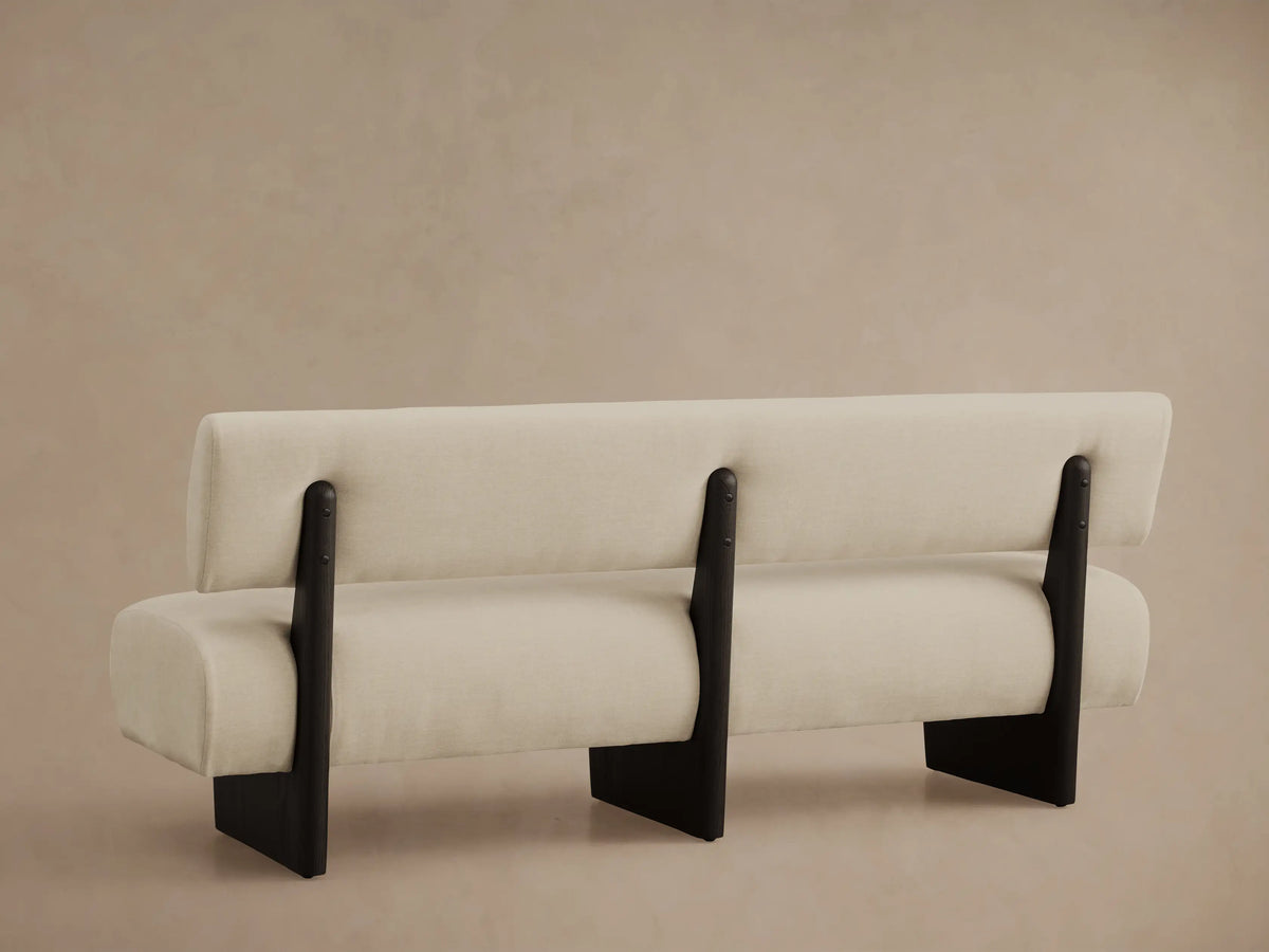 Close-up of a Beau Banquette with light beige textured fabric upholstery and a dark curved wooden armrest, viewed from above.