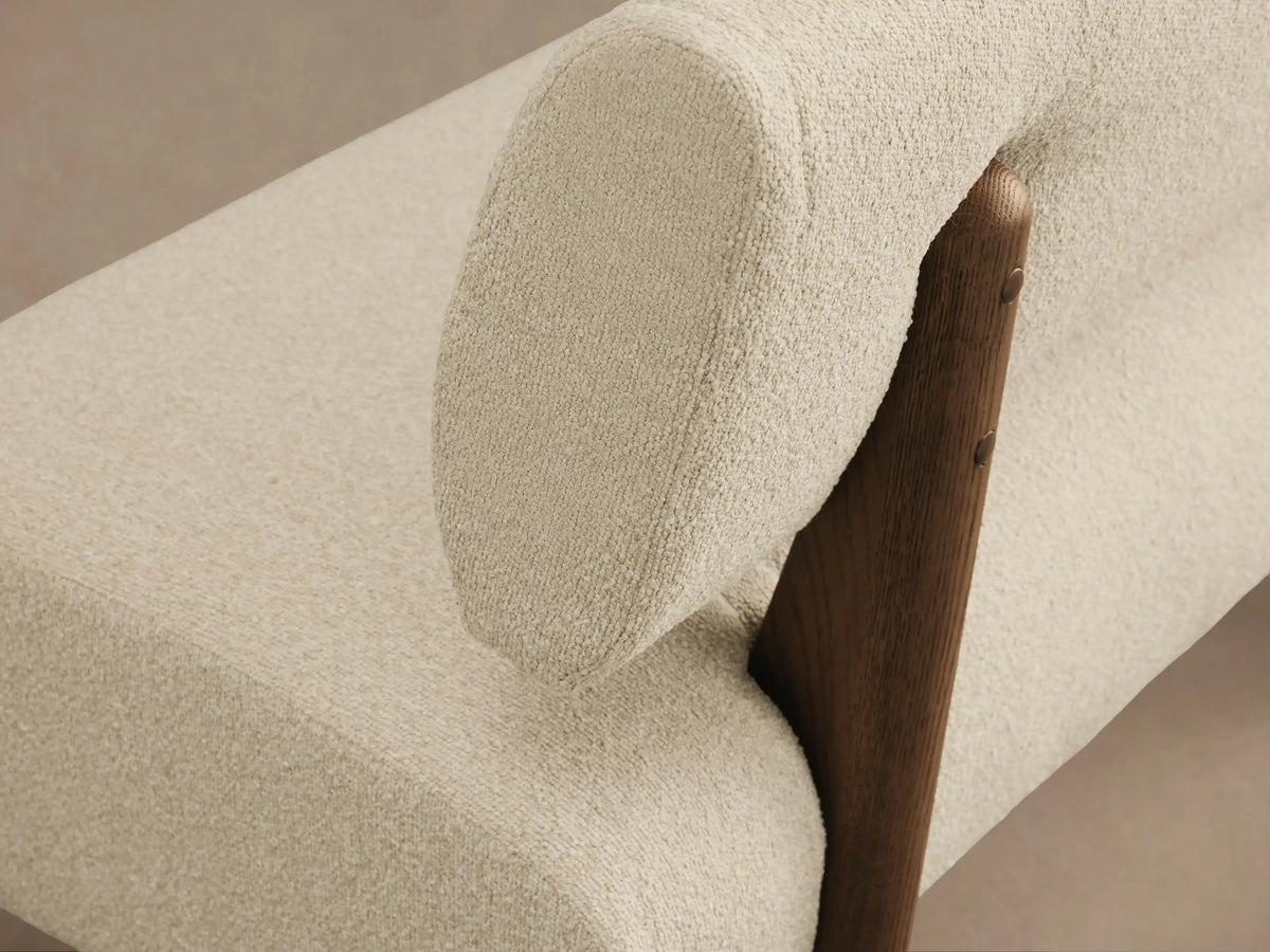 Beau Banquette: Cream boucl?? upholstered banquette with rounded backrest and dark wood base on a hardwood floor.