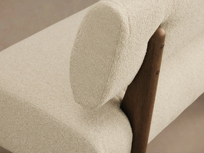 Beau Banquette: Cream boucl?? upholstered banquette with rounded backrest and dark wood base on a hardwood floor.