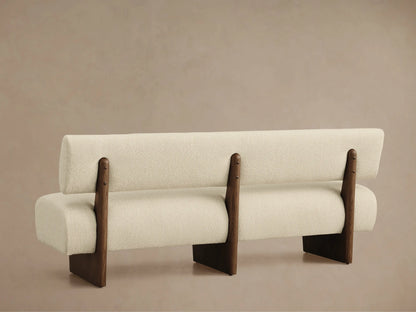 Angled top-down view of Beau Banquette. Cream textured boucle fabric with a curved backrest and dark wood frame detail.