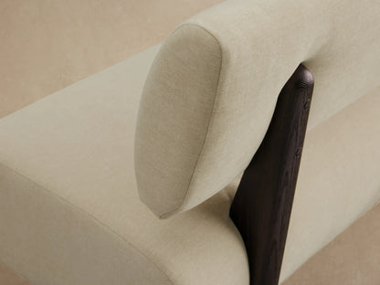 Modern Beau Banquette with light cream upholstery, straight backrest, and rounded seat, on dark angular legs on a wood floor.