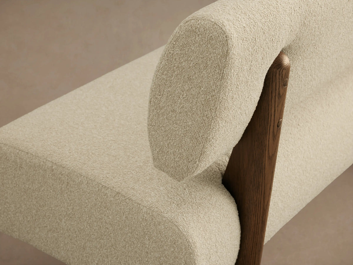 Long, off-white boucl?? upholstered banquette with curved seat & separate rectangular backrest, dark wood base.