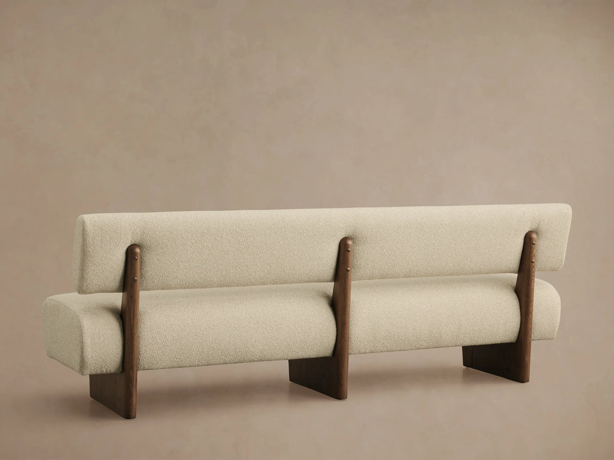 Close-up of Beau Banquette's textured light cream boucl?? fabric seat and rounded back, with a visible dark wood frame.