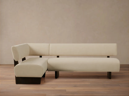 L-shaped Beau Banquette with cream upholstery and sleek dark wood base, set against a neutral wall on a wooden floor.