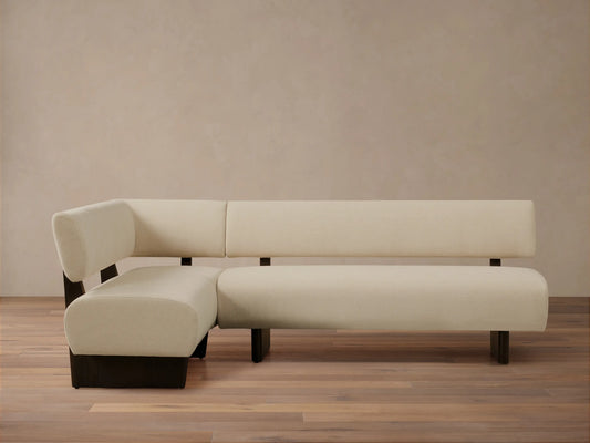 L-shaped Beau Banquette with cream upholstery and sleek dark wood base, set against a neutral wall on a wooden floor.