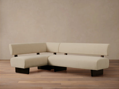 L-shaped Beau Banquette with cream upholstery and sleek dark wood base, set against a neutral wall on a wooden floor.