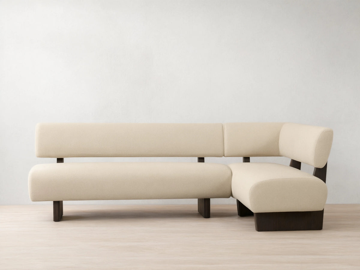L-shaped Beau Banquette with cream upholstery and sleek dark wood base, set against a neutral wall on a wooden floor.