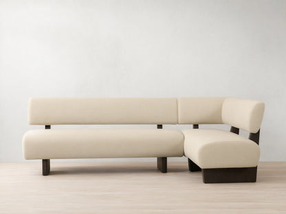 L-shaped Beau Banquette with cream upholstery and sleek dark wood base, set against a neutral wall on a wooden floor.