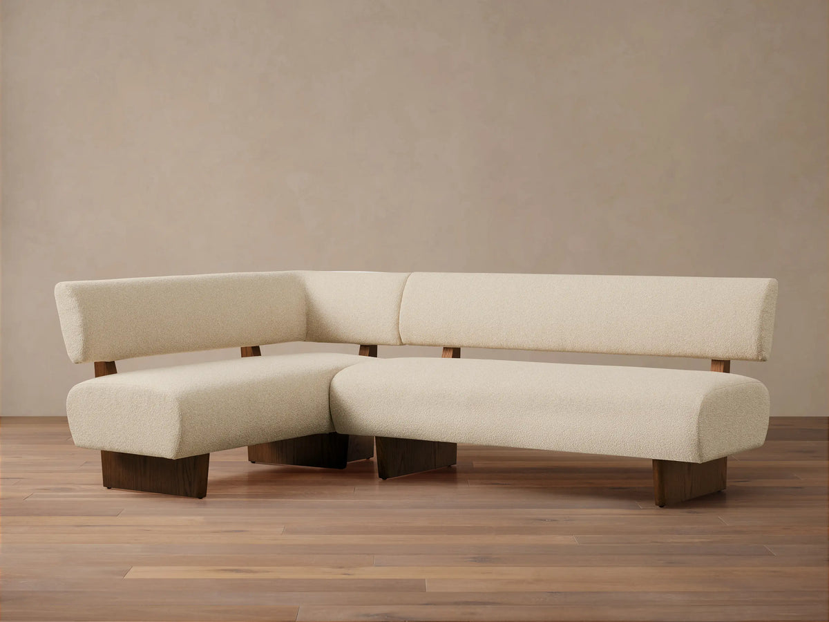L-shaped Beau Banquette in cream boucle fabric with dark wooden base and frame, on a wood floor against a neutral wall.
