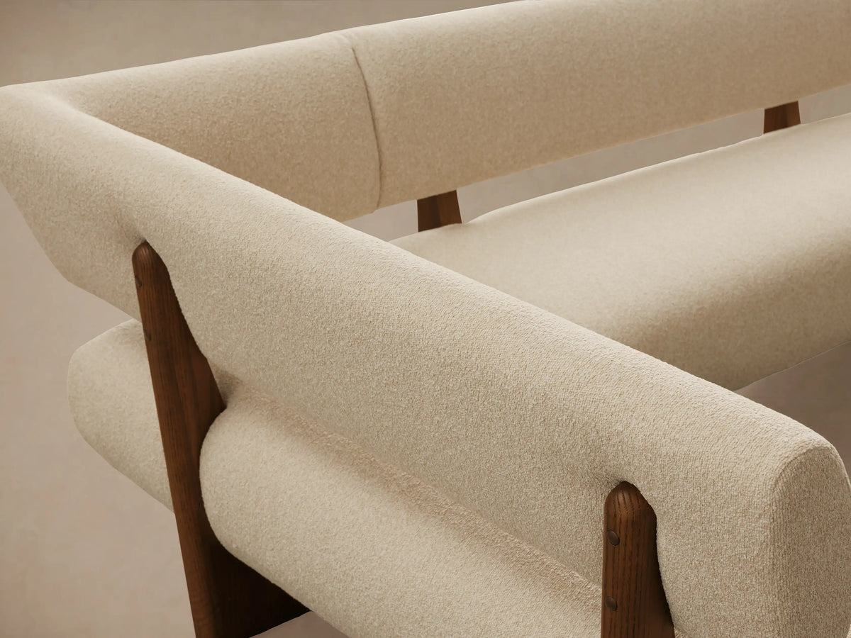 L-shaped Beau Banquette with cream bouclv© upholstery, supported by dark wood bases and backrests, on a light wooden floor.
