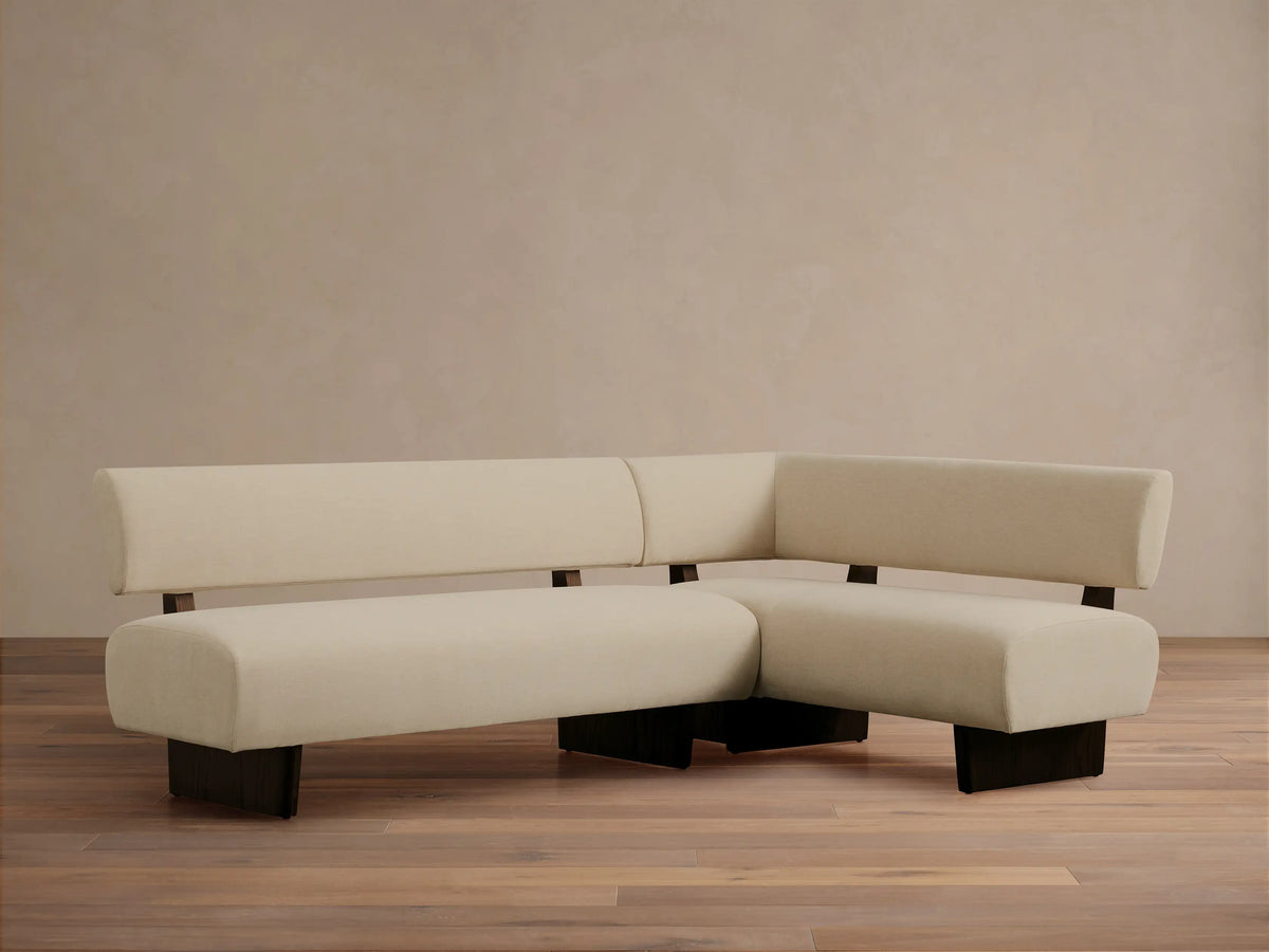 Beau Banquette, L-shaped, cream upholstery, and dark exposed wood frame, on a wooden floor.