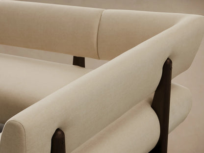 L-shaped cream Beau Banquette features thick upholstered cushions & dark oak veneer frame, on a wood floor.