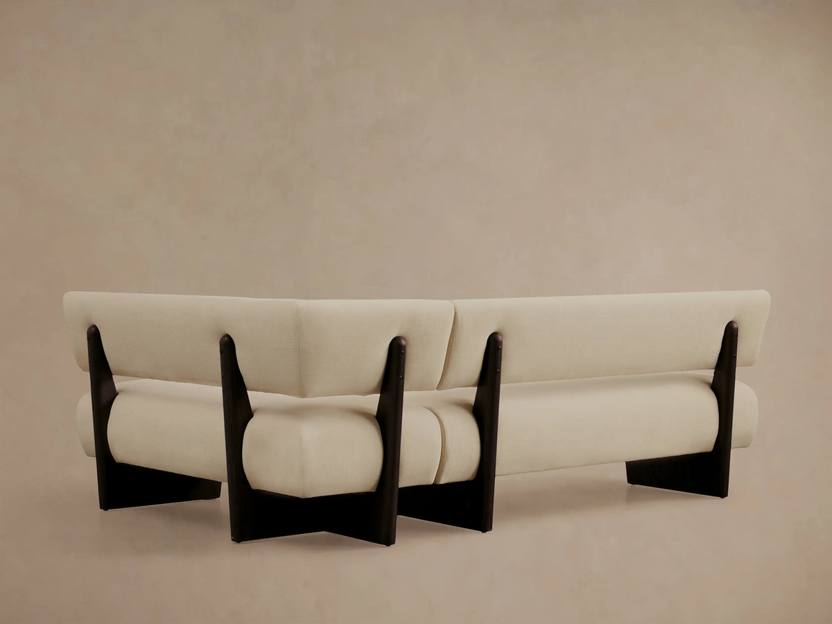 Beau Banquette, angled close-up. Light cream upholstery, dark brown exposed wood frame, showing modern curved lines.