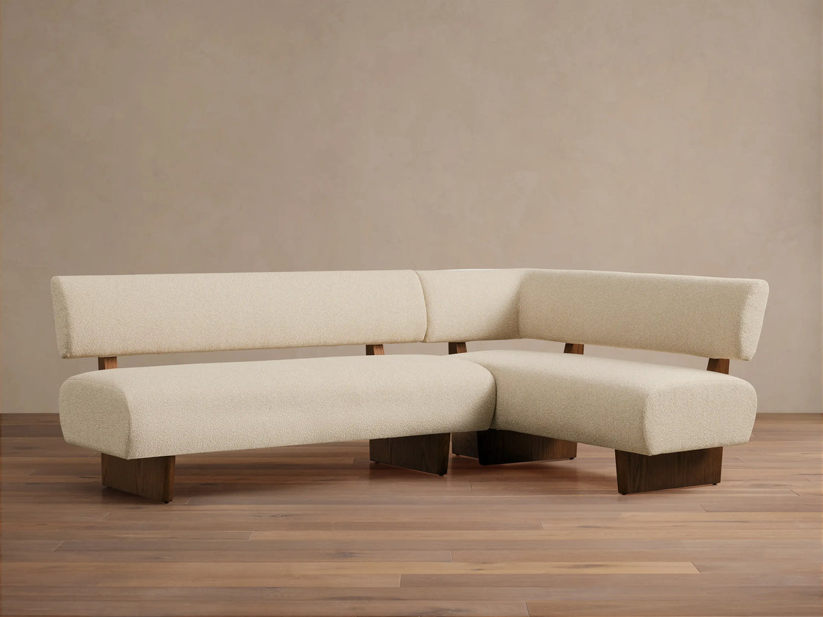 L-shaped Beau Banquette, cream boucle upholstery, low backrests, dark wood base, on a wooden floor against a neutral wall.