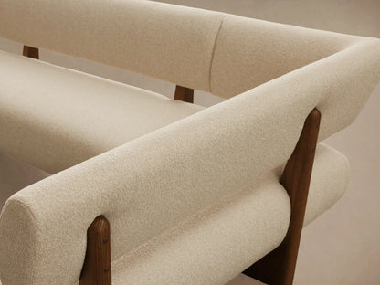 A cream, L-shaped Beau Banquette with textured upholstery and exposed dark wood frame, angled on a wooden floor.