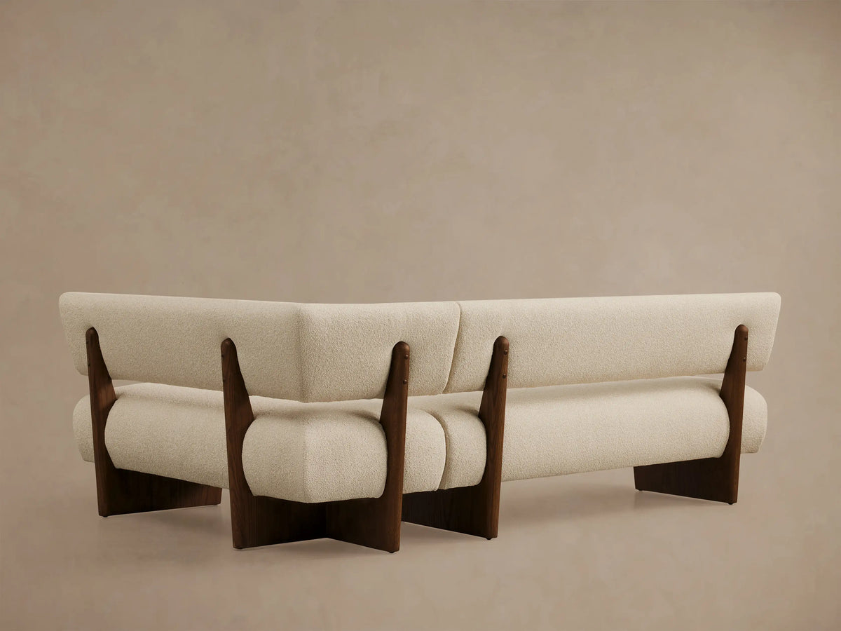 Beau Banquette: Angled view of light cream textured upholstery curving into a backrest and armrest on a dark wood frame.