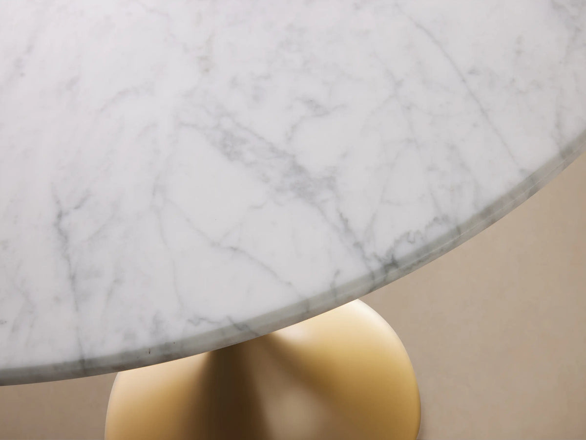 Round Saint Germain Bistro Table with a white Carrara marble tabletop and gold steel pedestal base on a wood floor background.