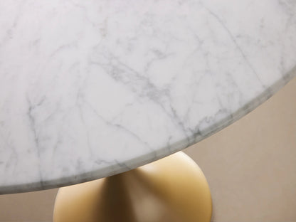 Round Saint Germain Bistro Table with a white Carrara marble tabletop and gold steel pedestal base on a wood floor background.
