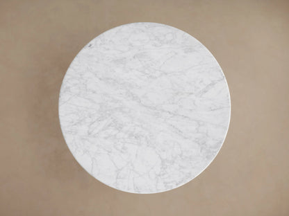 Saint Germain Bistro Table with round Carrara marble top and sleek dark steel base, on wooden floor against a beige wall.
