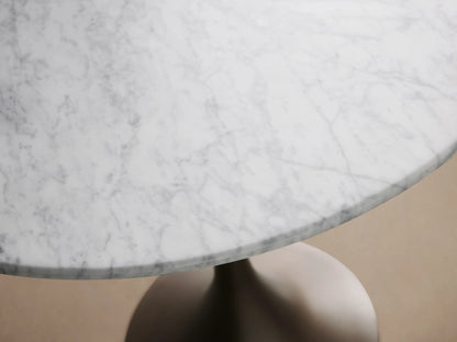 Saint Germain Bistro Table with a round white Carrara marble top and a sleek, dark brown pedestal steel base on wooden floor.