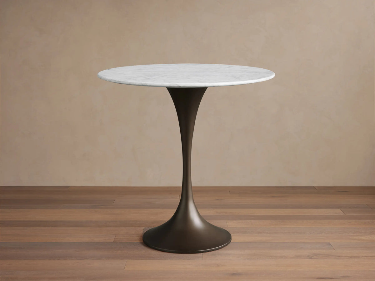 Round Carrara marble tabletop with light gray veining, resting on a metallic steel base. Marble surface shows natural patterns.