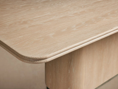 Caden Wood Dining Table, light sand-finished oak veneer with rounded rectangular top and solid pedestal base, on wood floor.