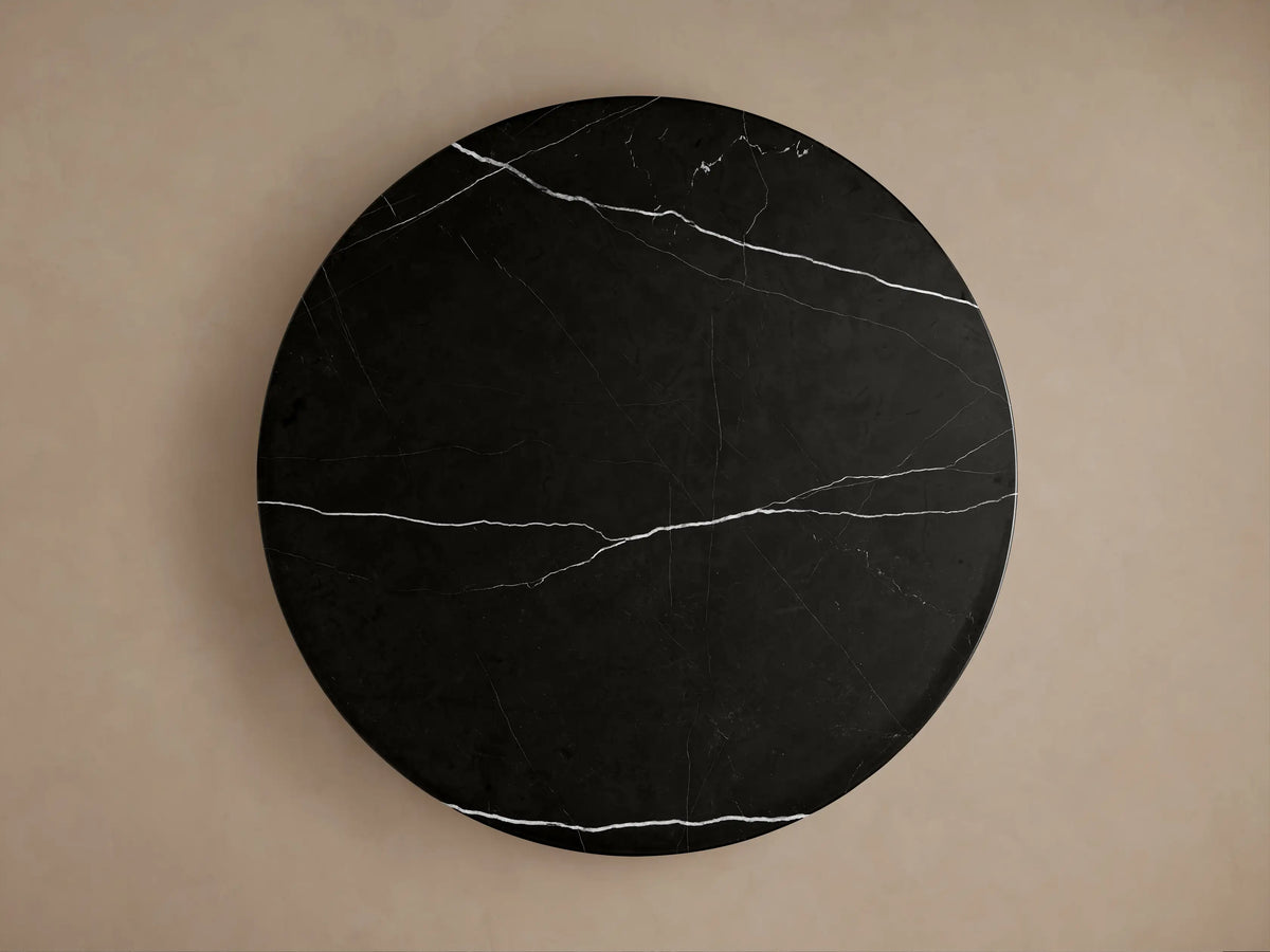 Close-up of Caden Round Dining Table with a black marble top featuring white veins, resting on a dark brown walnut wood base.
