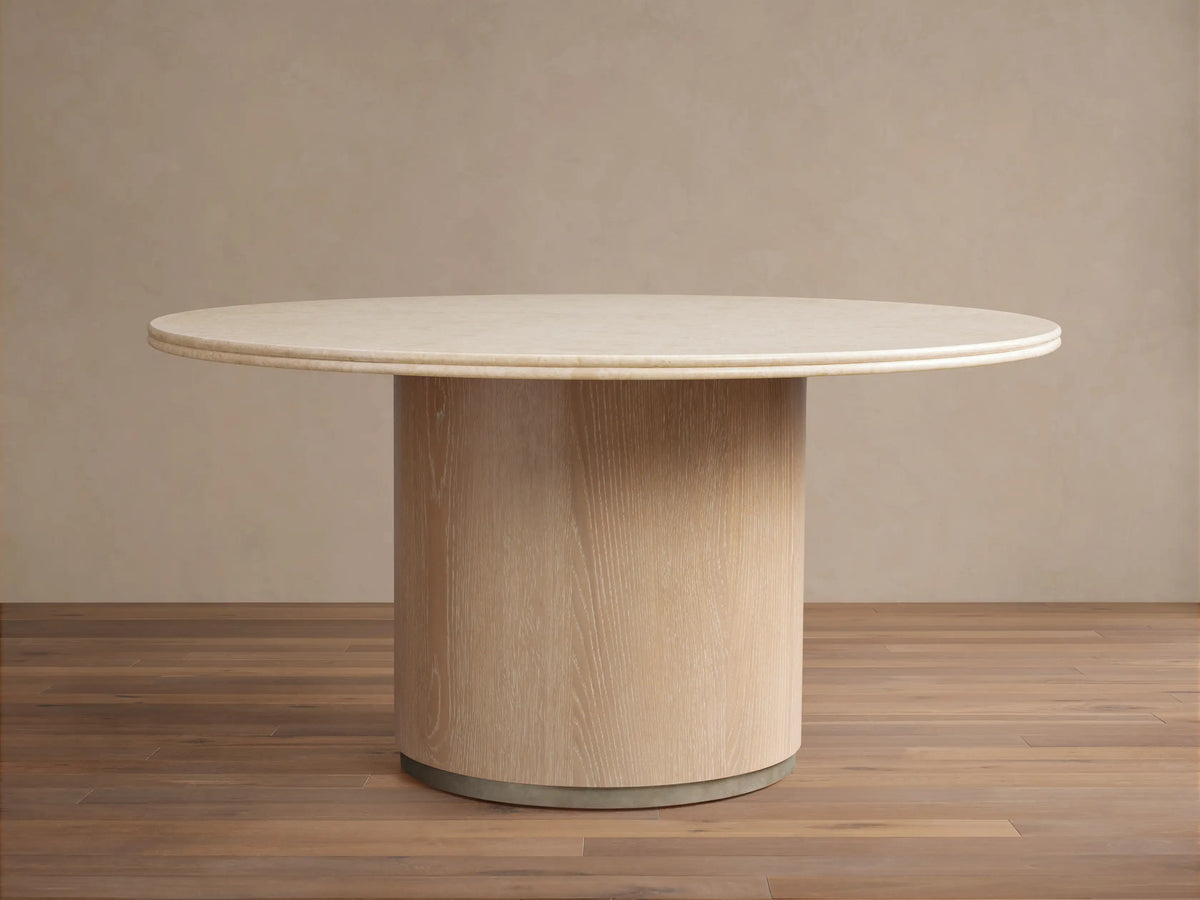 Caden Round Dining Table with a light-colored top and a cylindrical, sand-finished oak veneer base on a wood floor.