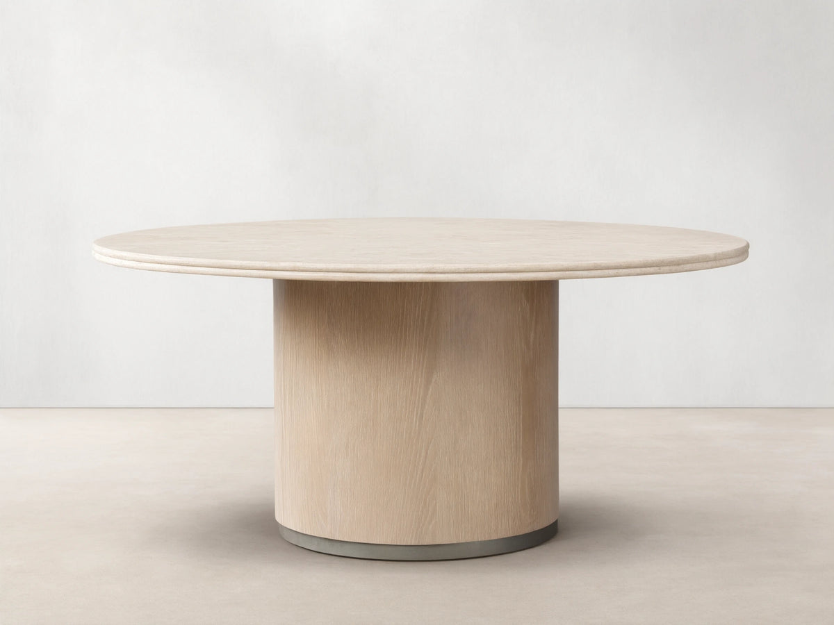 Caden Round Dining Table with a light-colored top and a cylindrical, sand-finished oak veneer base on a wood floor.