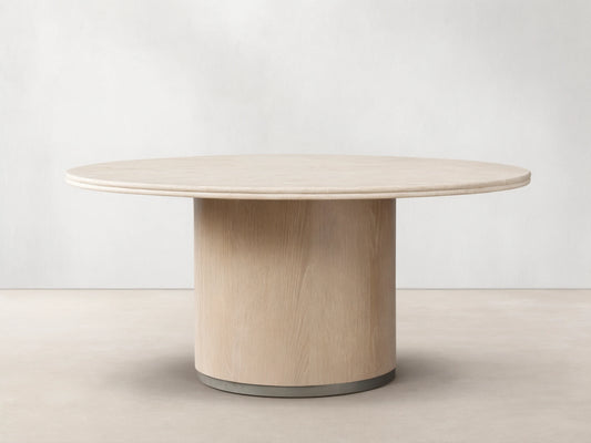 Caden Round Dining Table with a light-colored top and a cylindrical, sand-finished oak veneer base on a wood floor.