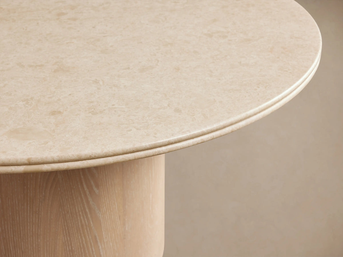 Caden Round Dining Table with a light-colored top and a cylindrical, sand-finished oak veneer base on a wood floor.