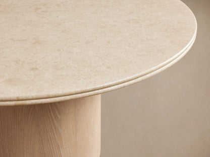 Caden Round Dining Table with a light-colored top and a cylindrical, sand-finished oak veneer base on a wood floor.