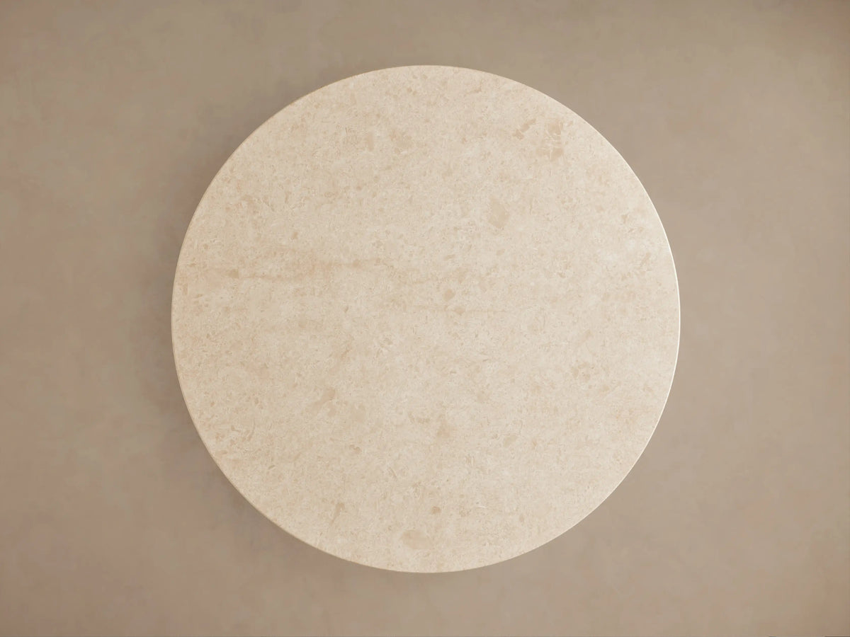 Caden Round Dining Table with a light, speckled stone top over a light oak veneer pedestal base, angled view.