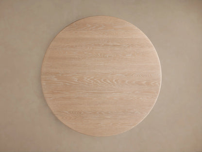 Close-up of a Caden Round Wood Dining Table. It has a light sand finish, detailed wood grain, and a thick round top on a cylindrical base.