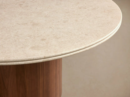 Caden Round Dining Table: round light sand stone top, dark walnut cylindrical wood base on a wood floor.