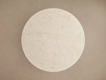 Close-up of Caden Round Dining Table. Round, light beige stone top with subtle texture, resting on a rich brown wood cylindrical base.