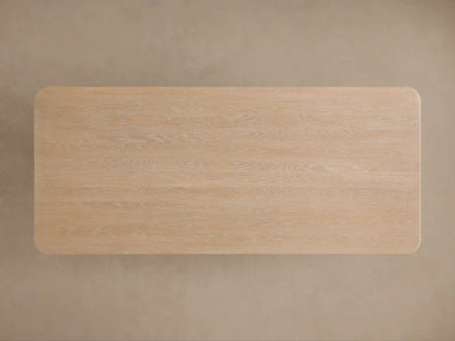 Light sand finish Caden Wood Dining Table with visible oak veneer grain, rounded corner, and curved support base.