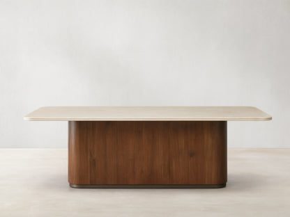 Caden Dining Table with a light, rectangular stone top and a dark walnut wood pedestal base, on a wooden floor.