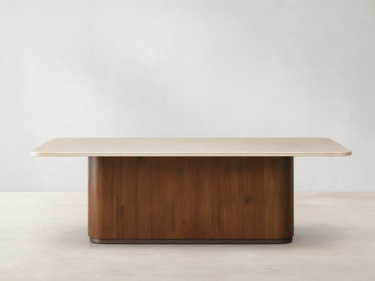 Caden Dining Table with a light, rectangular stone top and a dark walnut wood pedestal base, on a wooden floor.