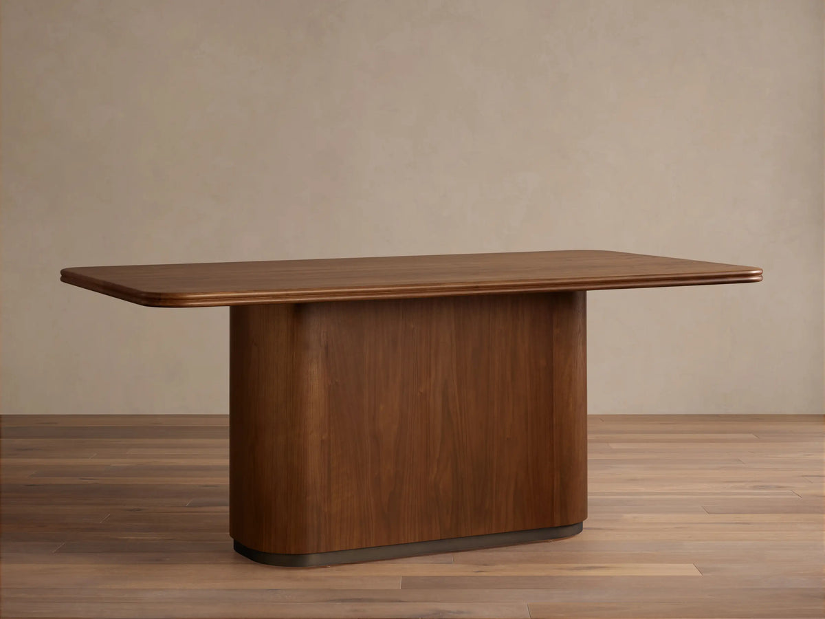 Caden Wood Dining Table: Rectangular top with rounded corners, solid pedestal base, rich walnut wood finish.