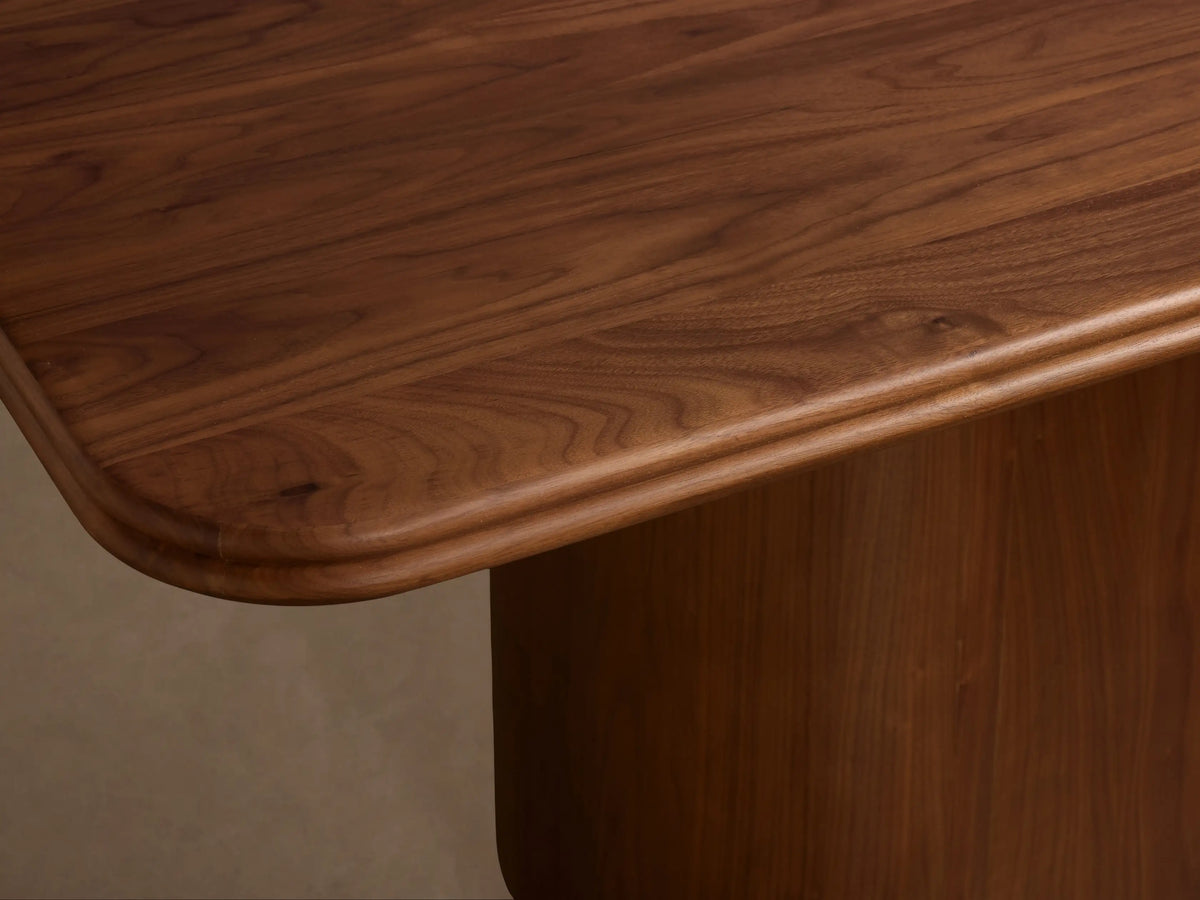 Caden Wood Dining Table with a smooth dark walnut rectangular top & rounded edges, supported by a curved pedestal base.