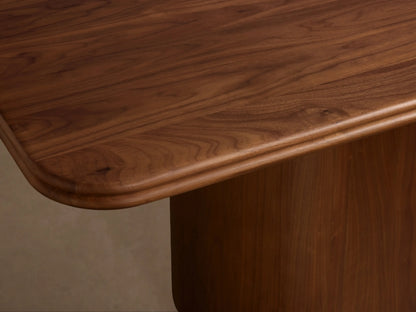 Caden Wood Dining Table with a smooth dark walnut rectangular top & rounded edges, supported by a curved pedestal base.