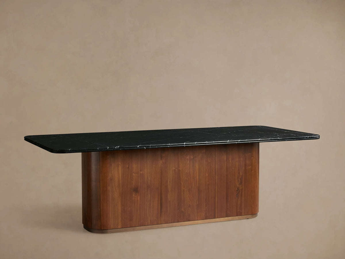 Caden Dining Table with a black marquina stone top, rectangular shape, resting on an American walnut wood base, in a warm setting.