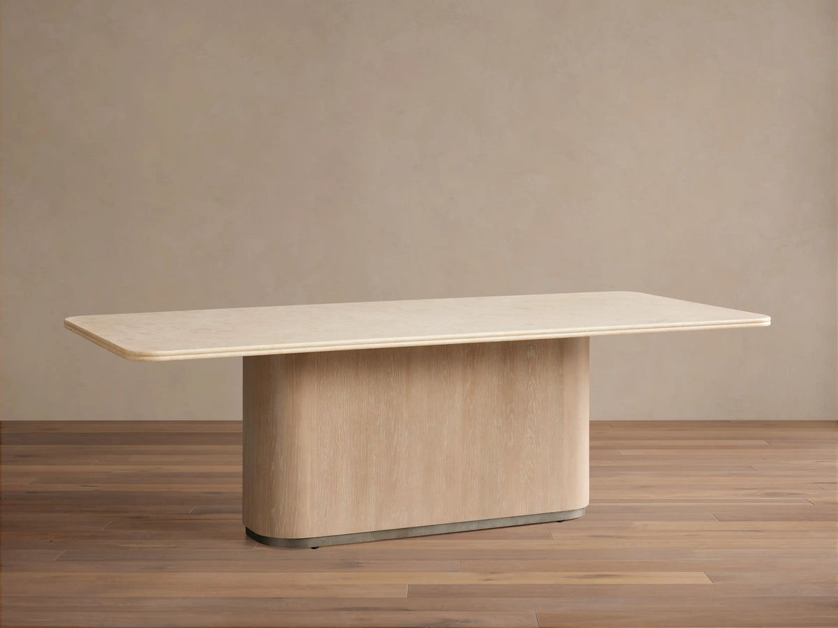 Caden Dining Table: Rectangular light top with rounded corners, light oak veneer pedestal base. On wood floor, against beige wall.