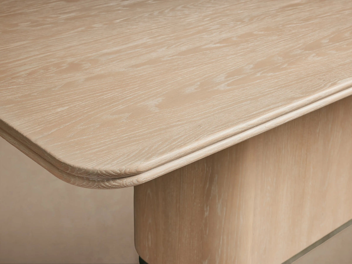 Caden Wood Dining Table, light sand finish with rounded rectangular top & solid pedestal base on wood floor.