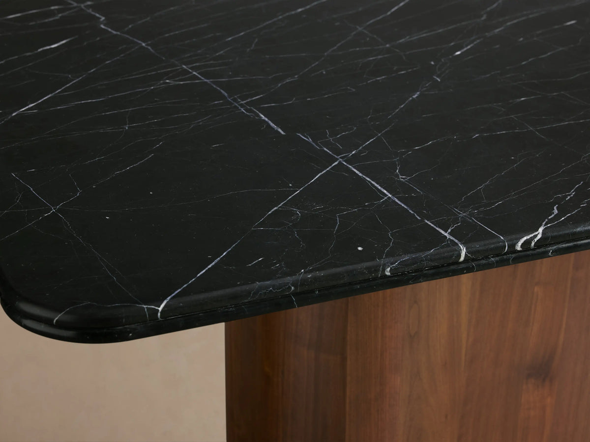 Caden Dining Table with a rectangular black marquina stone top and rounded American walnut wood veneer base, set against a plain background.