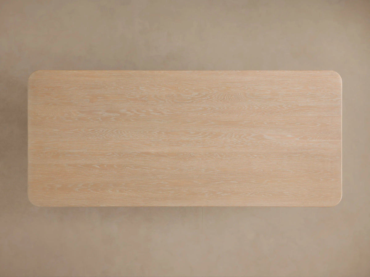 Close-up of Caden Wood Dining Table corner. Light sand oak veneer top with rounded edge and matching curved leg.