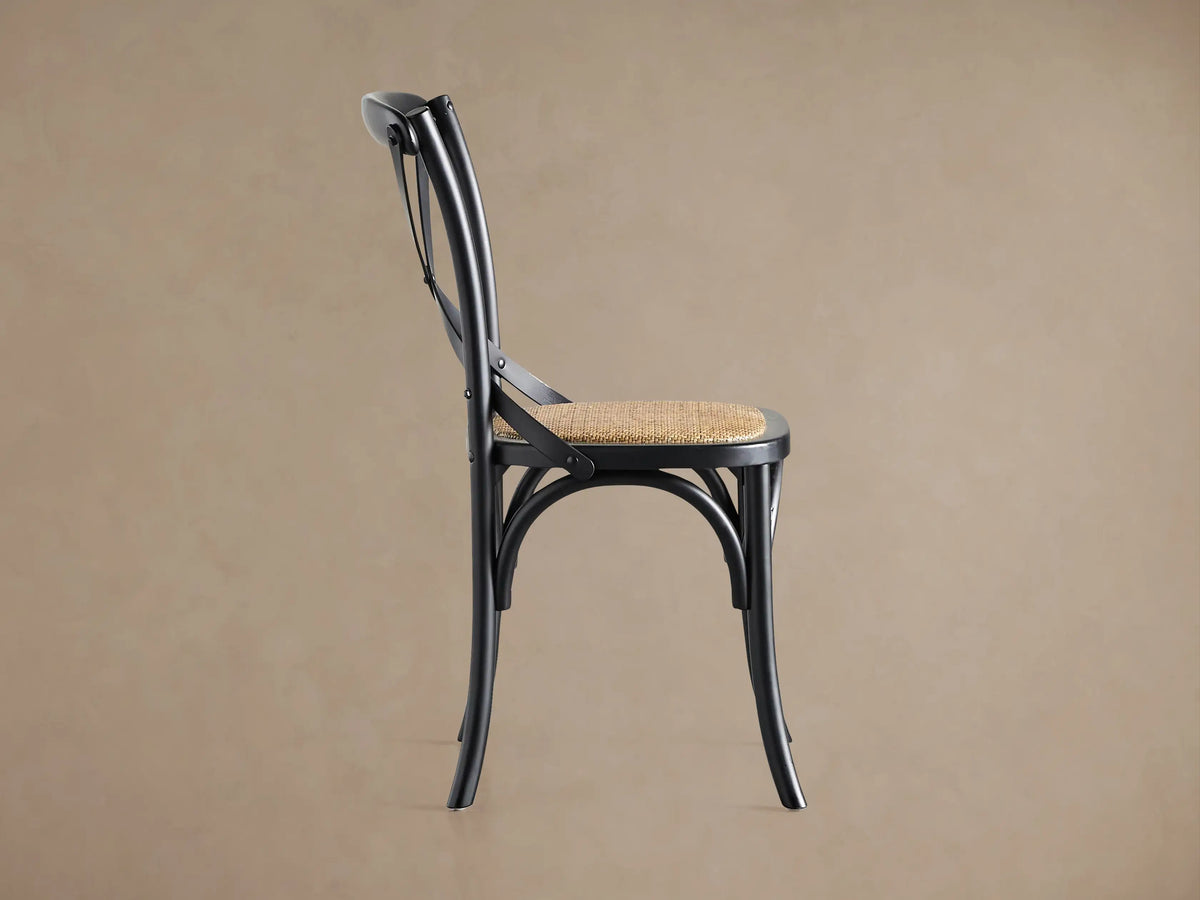 Cadence Dining Chair in solid black birch, cross-back, and handwoven rattan seat, shown from a rear 3/4 angle.