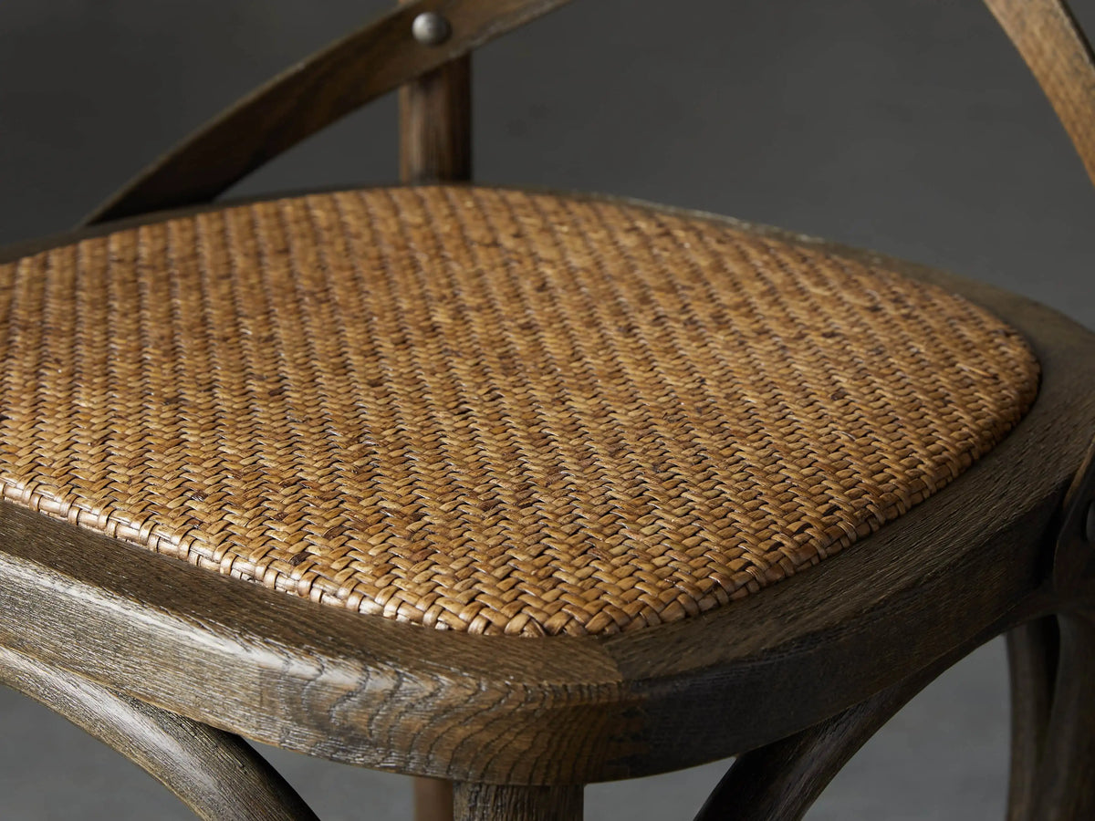 Dark weathered oak Cadence Stool with X-back and round rattan seat, front view on a gray background.