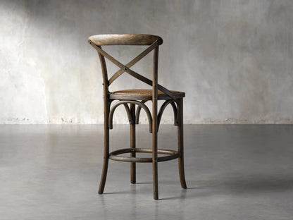 Close-up of Cadence Stool's dark brown weathered oak cross-back, showing wood grain and metal rivets against a dark background.